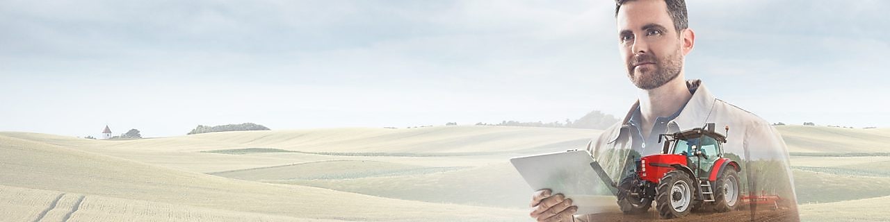 homme lisant un document dans un champ avec un tracteur rouge