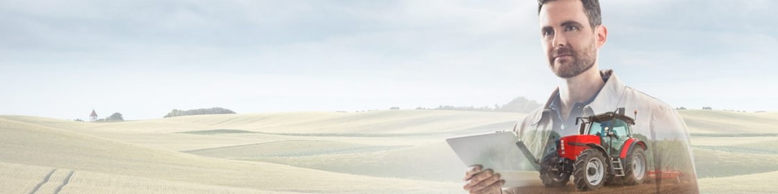 homme lisant un document dans un champ avec un tracteur rouge