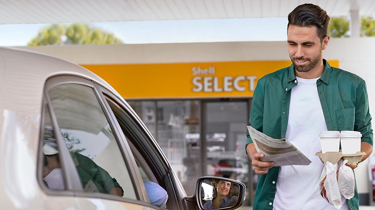 Automobilistes souriant qui revient d'un shop shell select avec ses achats
